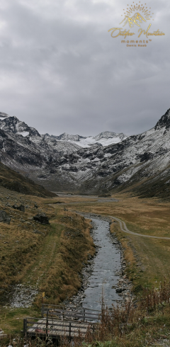 Berge Berglandschaft mit einem Fluss, grünen Wiesen und schneebedeckten Gipfeln.