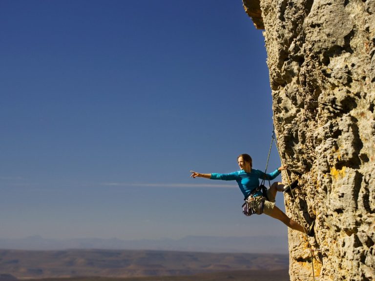 Kletterin Ein Kletterer balanciert an einer steilen Felswand unter blauem Himmel.